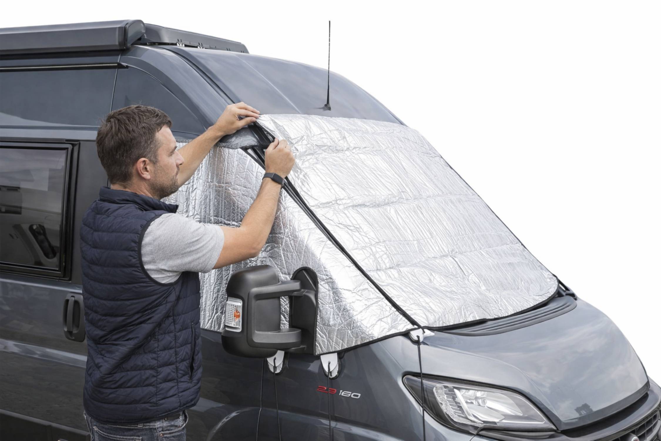 Eine Person installiert eine reflektierende Sonnenblende auf der Windschutzscheibe eines Vans, um das Innere vor Hitze und Sonnenlicht zu schützen.