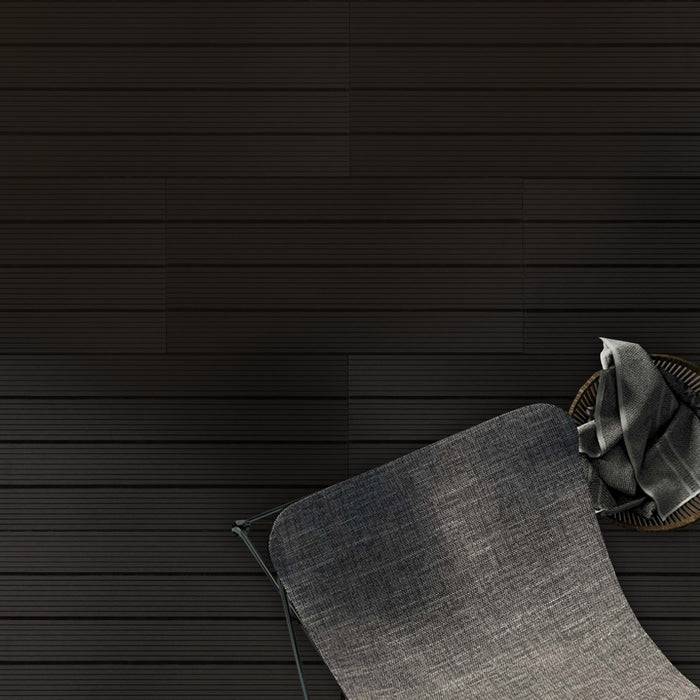 Ein dunkelgrauer gewebter Stoff-Stuhl mit teilweise sichtbaren Metallfüßen auf der linken Seite, vor einem horizontalen strukturierten schwarzen Hintergrund.