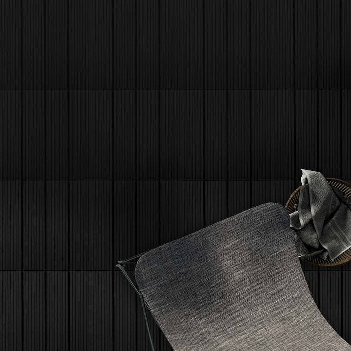 Ein grauer Stoffsessel mit einem gefalteten grauen Tuch auf seiner Armlehne steht vor einer strukturierten schwarzen Wand und schafft damit ein minimalistisches und modernes Aussehen.