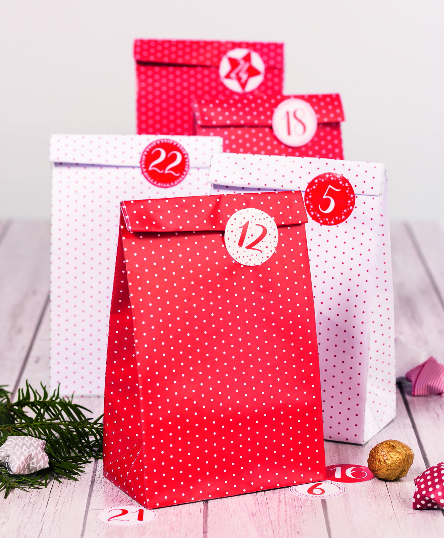 Bunte, gepunktete Geschenktüten mit nummerierten Kreisen auf einer Holzoberfläche angeordnet, was auf einen festlichen Countdown oder Adventskalender hindeutet.