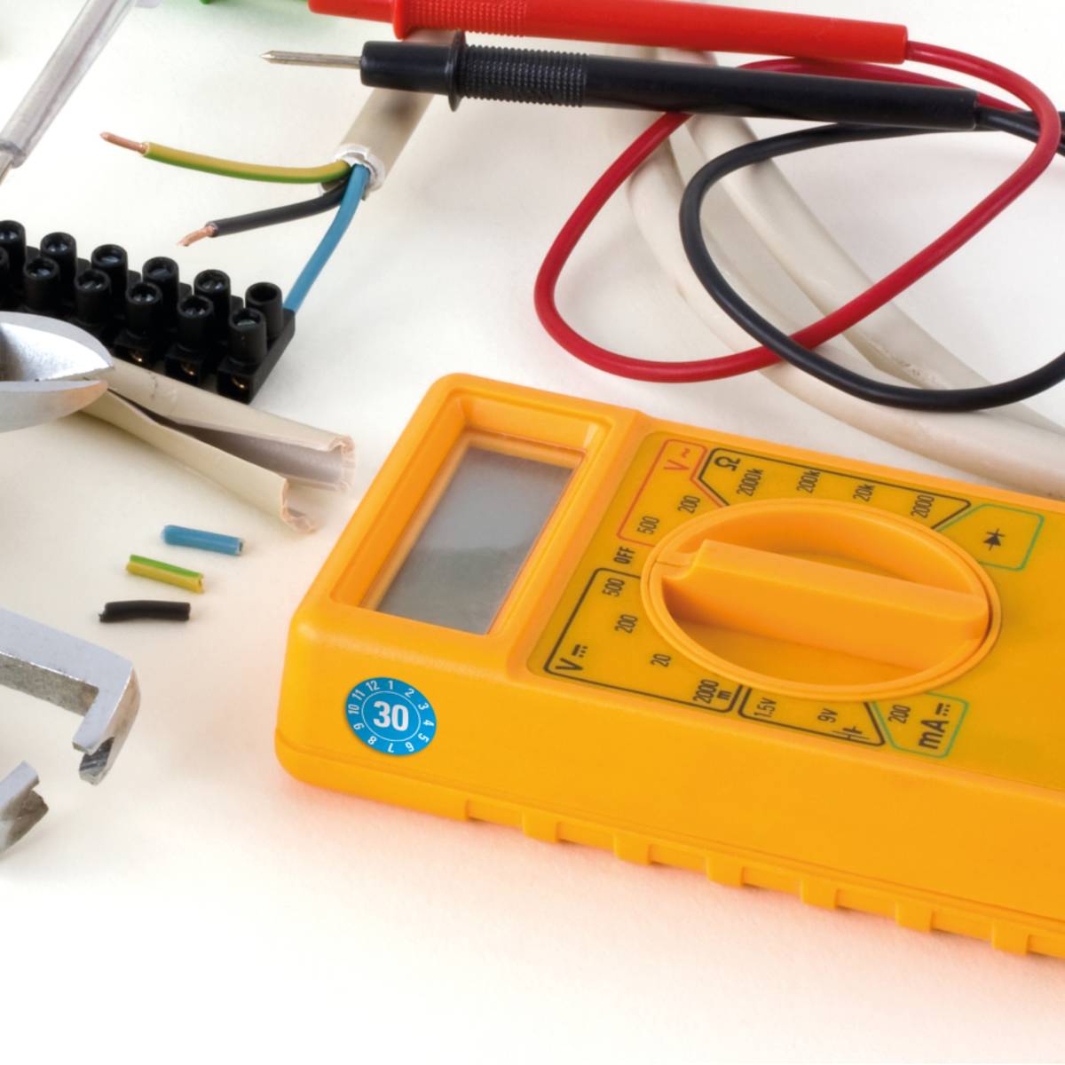Ein gelbes digitales Multimeter mit Messleitungen und verschiedenen elektrischen Werkzeugen, was auf einen Schwerpunkt auf elektrische Prüfungen oder Reparaturarbeiten hindeutet.