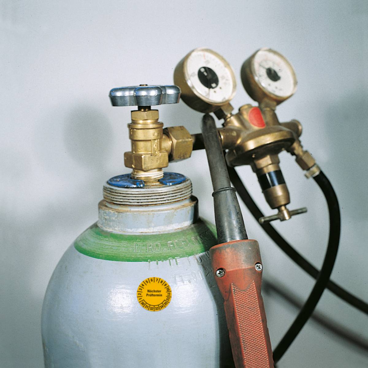 Ein Gaszylinder mit angebrachten Druckmessern und einem angeschlossenen Schlauch, der zur Regulierung und Überwachung des Gasflusses in industriellen Anwendungen verwendet wird.