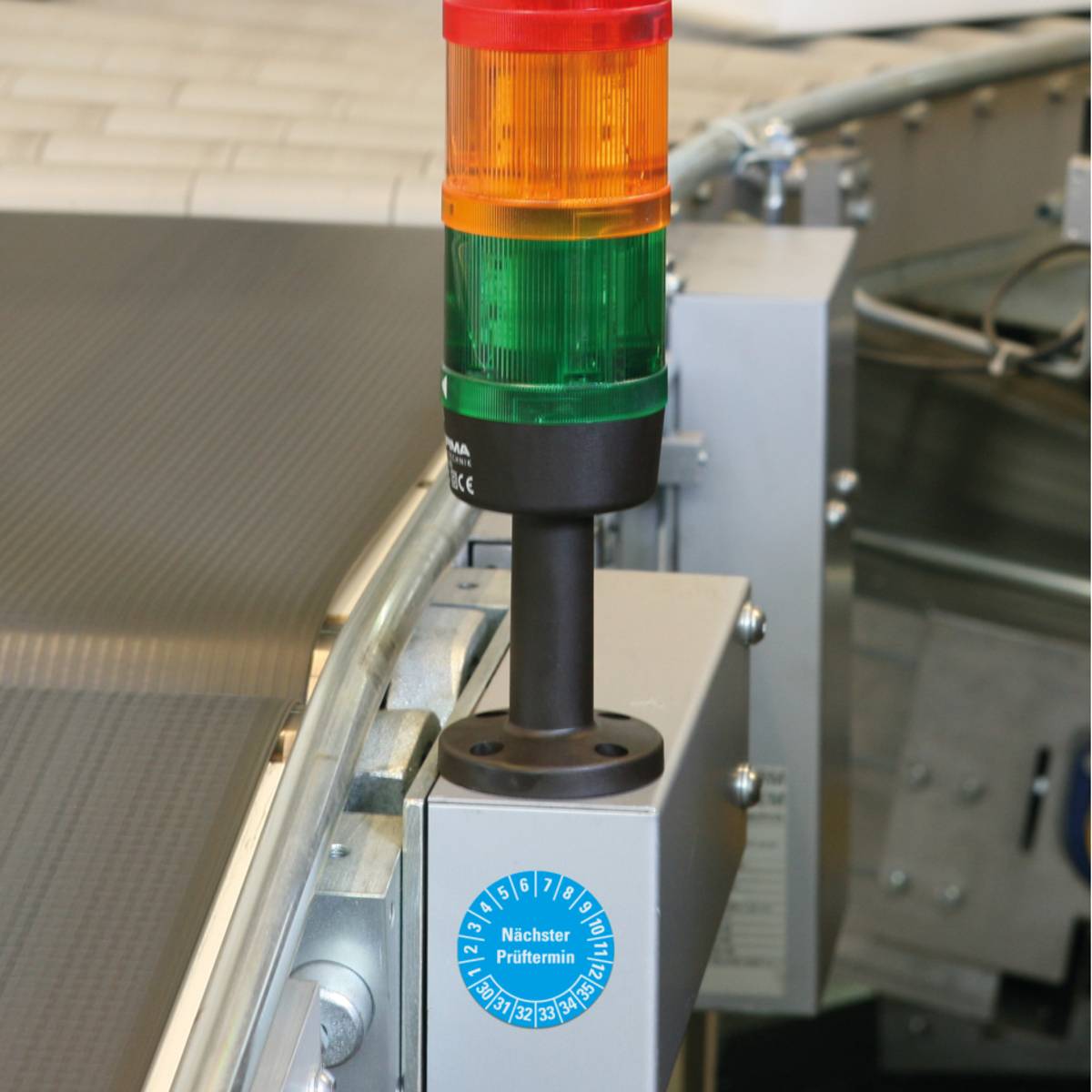 Bild eines Stapellichts mit roten, orangefarbenen und grünen Lichtern auf einem Förderbandsystem, das den Maschinenstatus oder Warnmeldungen anzeigt.