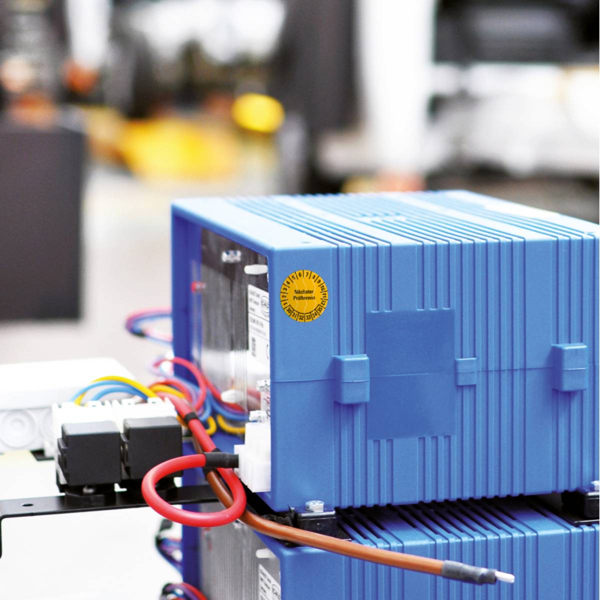 Eine Nahaufnahme eines blauen industriellen elektronischen Geräts mit Drähten und Steckverbindern, angebracht auf einer Metalloberfläche in einer unscharfen Werkstattumgebung.