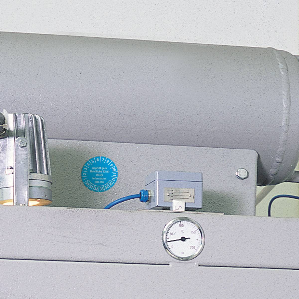 Ein Druckmessgerät für industrielle Anwendungen, das auf einer Metallmaschine mit einem Zylindertank im Hintergrund montiert ist.