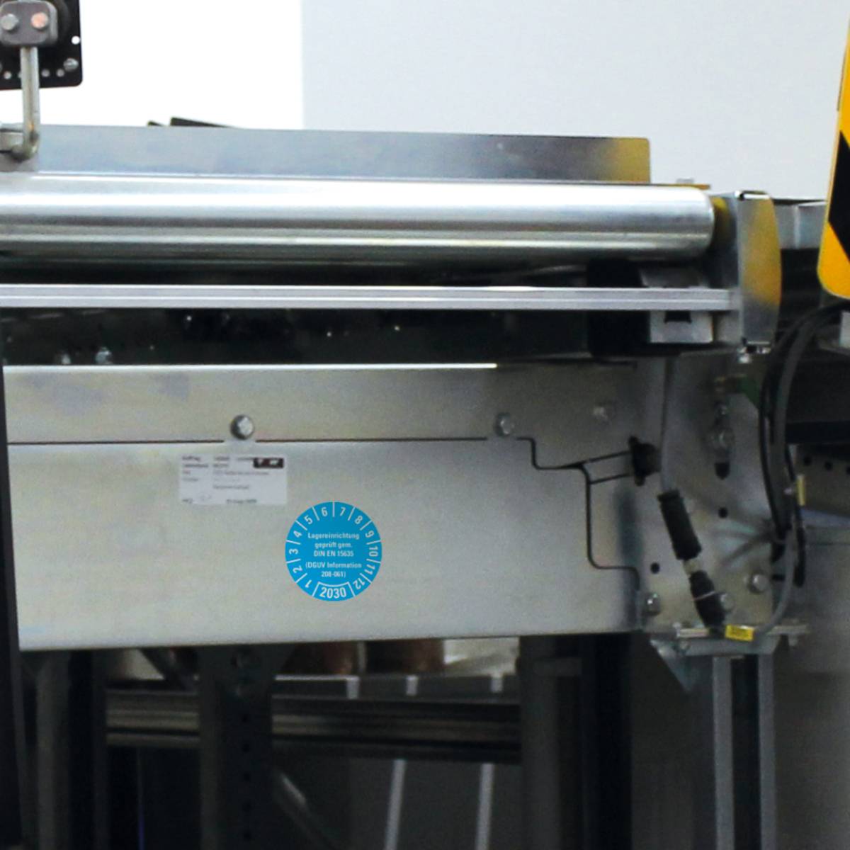 Eine Maschine mit Metallwalzen, die in einer industriellen Umgebung zur Materialverarbeitung verwendet wird. Auf ihrer Oberfläche befindet sich ein blauer runder Aufkleber.