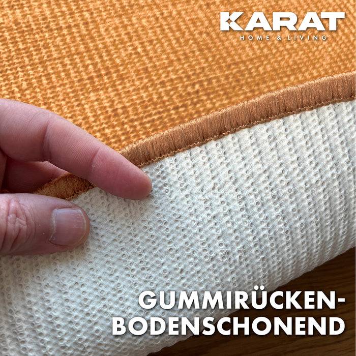 Eine Hand hebt einen strukturierten Teppich an und zeigt eine rutschfeste Gummirückseite. Der Text lautet „Gummirücken, bodenschonend