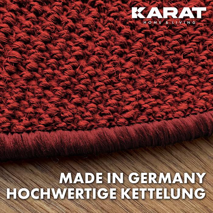 Nahaufnahme eines roten strukturierten Teppichs mit dicker Stickererei auf einer Holzoberfläche. Der Text lautet „Made in Germany Hochwertige Kettelung