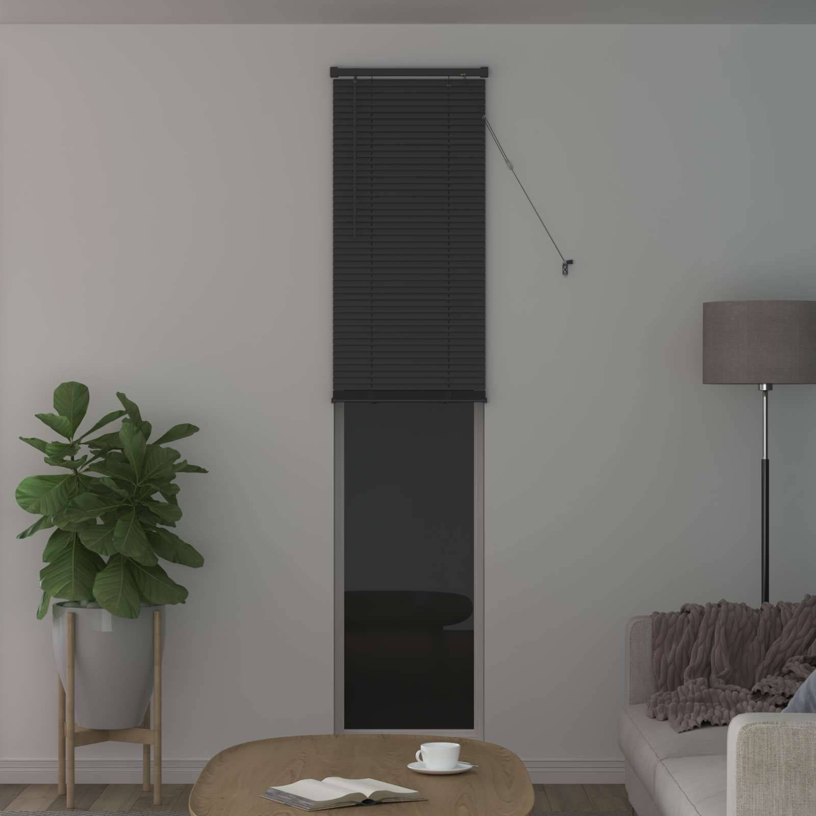 Ein modernes Wohnzimmer mit einem grauen Sofa, einer Topfpflanze, einer Stehleuchte und einem Fenster mit geschlossenen schwarzen Jalousien. Ein kleiner runder Couchtisch steht davor.