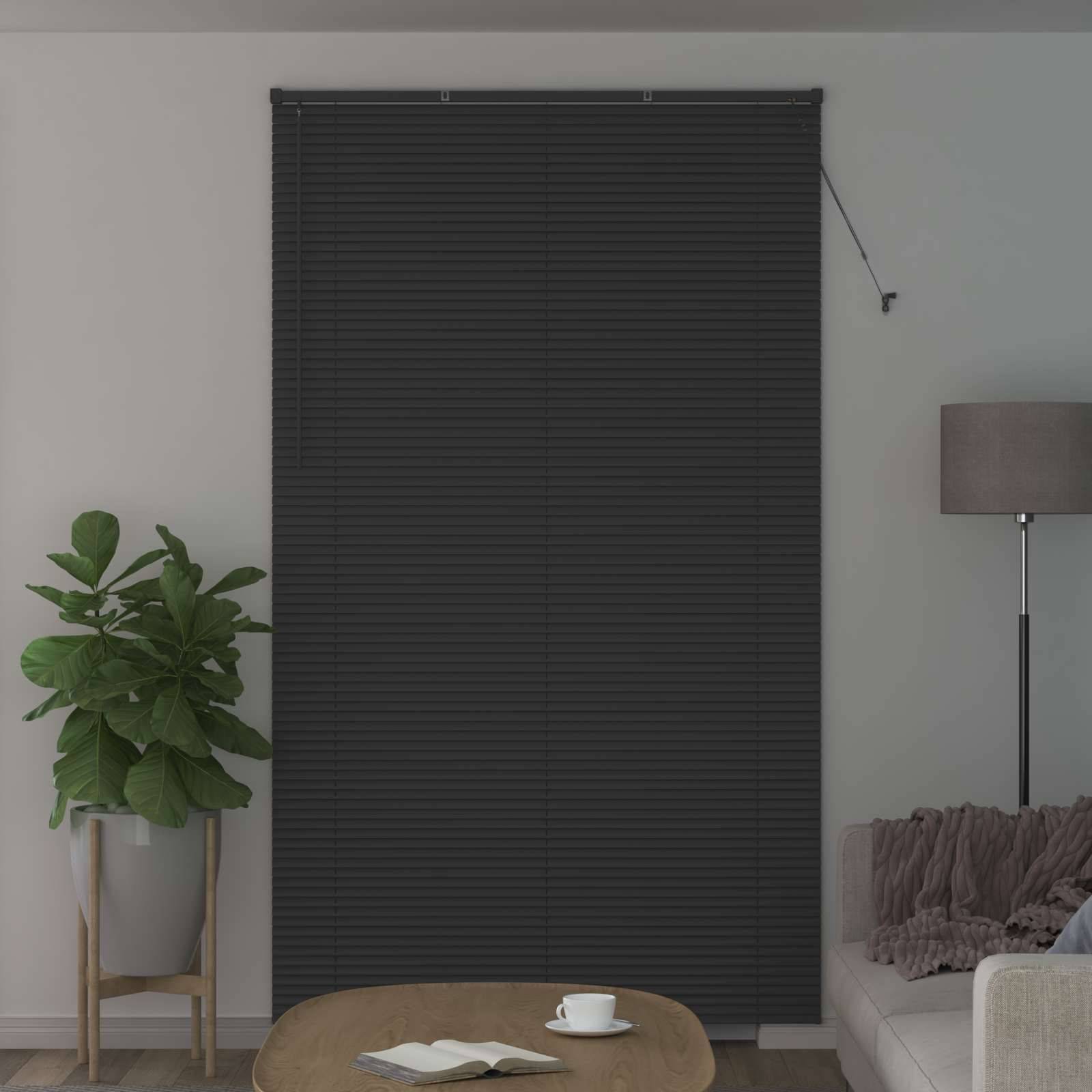 Ein gemütliches Wohnzimmer mit einer geschlossenen dunklen Fensterrollo, einer hohen Zimmerpflanze, einer Lampe und einem Sofa mit Kissen. Eine Tasse steht auf dem Tisch.