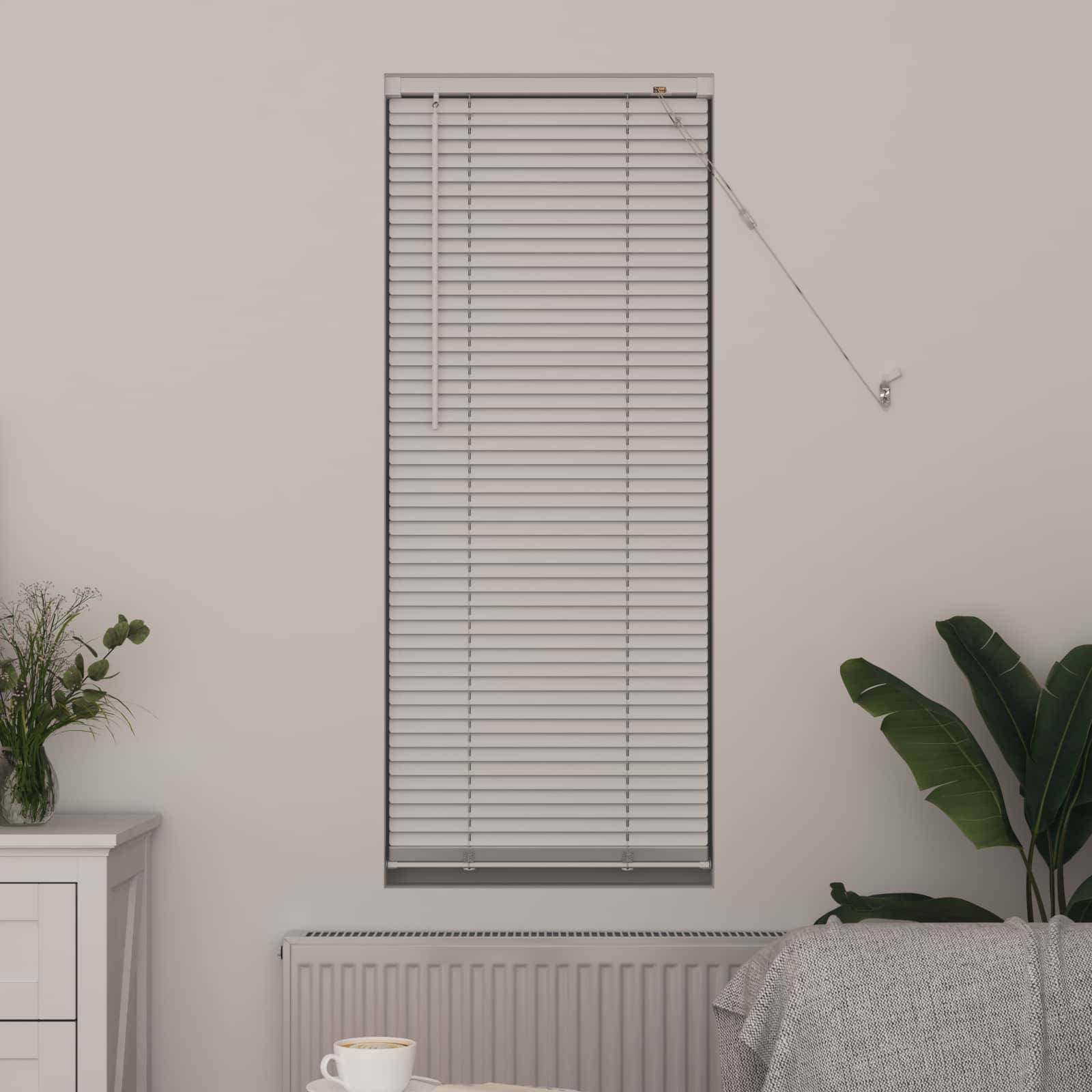 Ein geschlossenes Fensterrollo bedeckt ein kleines vertikales Fenster über einem Heizkörper. Eine weiße Tasse steht auf einer Kommode auf der linken Seite; eine grüne Pflanze auf der rechten Seite.