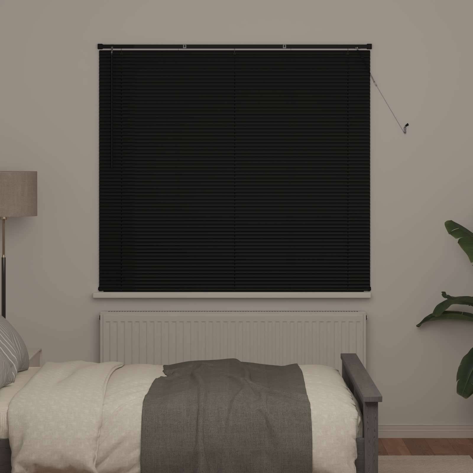 Ein Schlafzimmer mit einem Bett, einer gemusterten Decke und einer Lampe auf der linken Seite. Schwarze Jalousien bedecken ein Fenster über einem Heizkörper an einer beigefarbenen Wand.