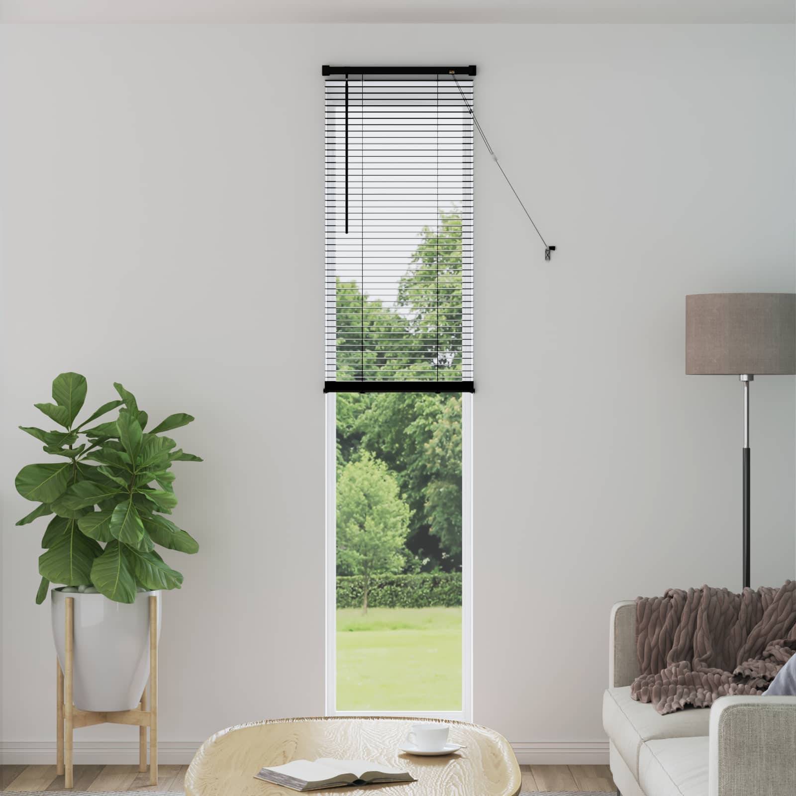 Ein minimalistisches Wohnzimmer mit einem Fenster, das grünes Laub draußen zeigt, eine Pflanze auf der linken Seite, eine hohe Stehlampe auf der rechten Seite und ein Tisch mit einem Buch davor.
