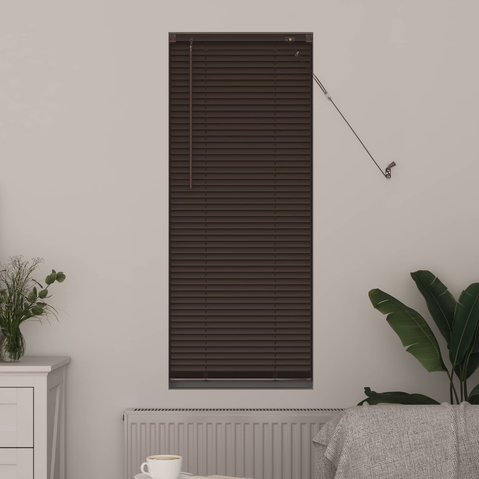 Ein braunes Fensterrollo ist vollständig geschlossen, mit einer Zugschnur, die auf der rechten Seite hängt. Darunter ist ein Heizkörper teilweise sichtbar, mit einer Topfpflanze auf der linken Seite.