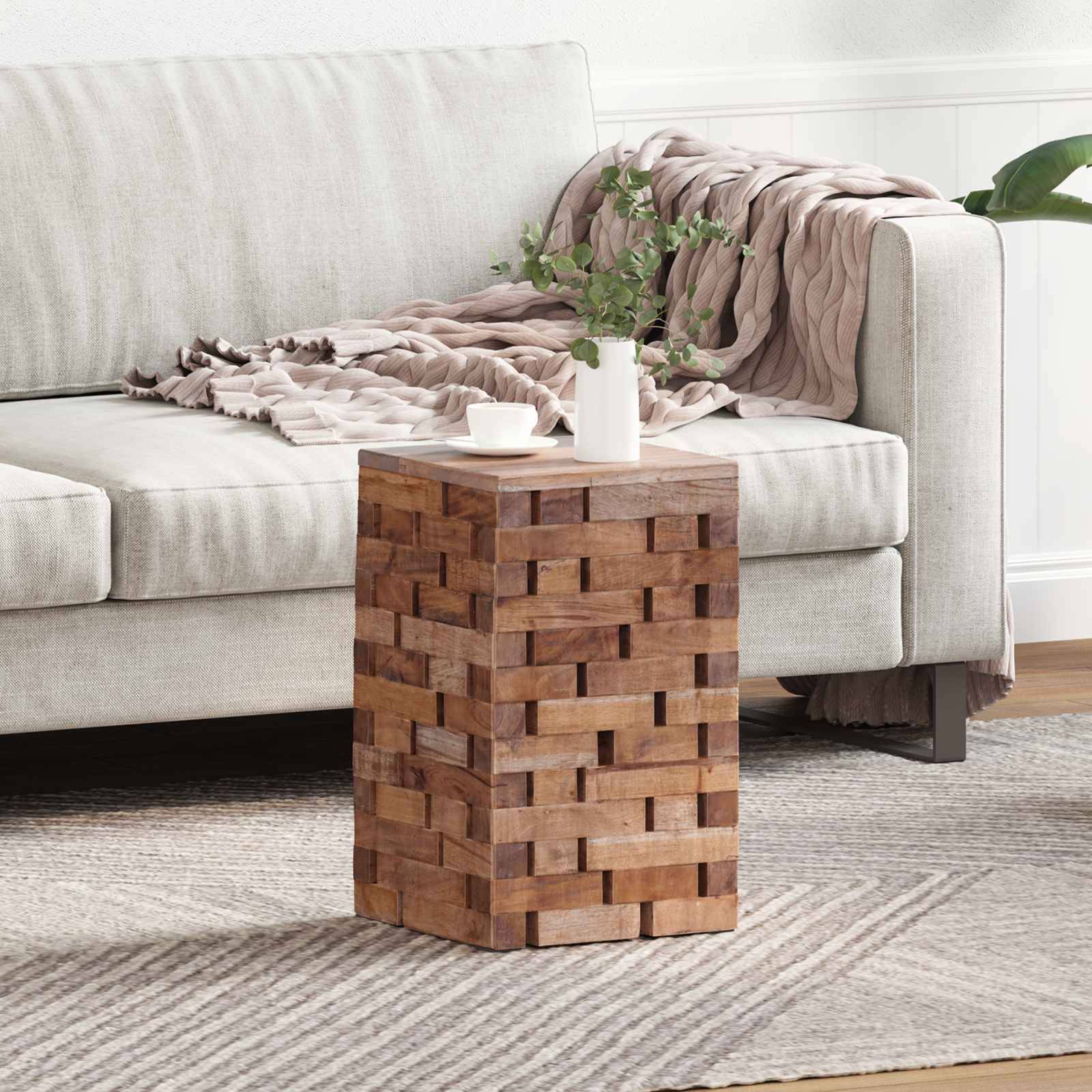 Ein gemütliches Wohnzimmer mit einem hellgrauen Sofa, einer beigen Wurfdecke, einem Holzbeistelltisch und einer kleinen Pflanze in einem weißen Topf zur Dekoration.