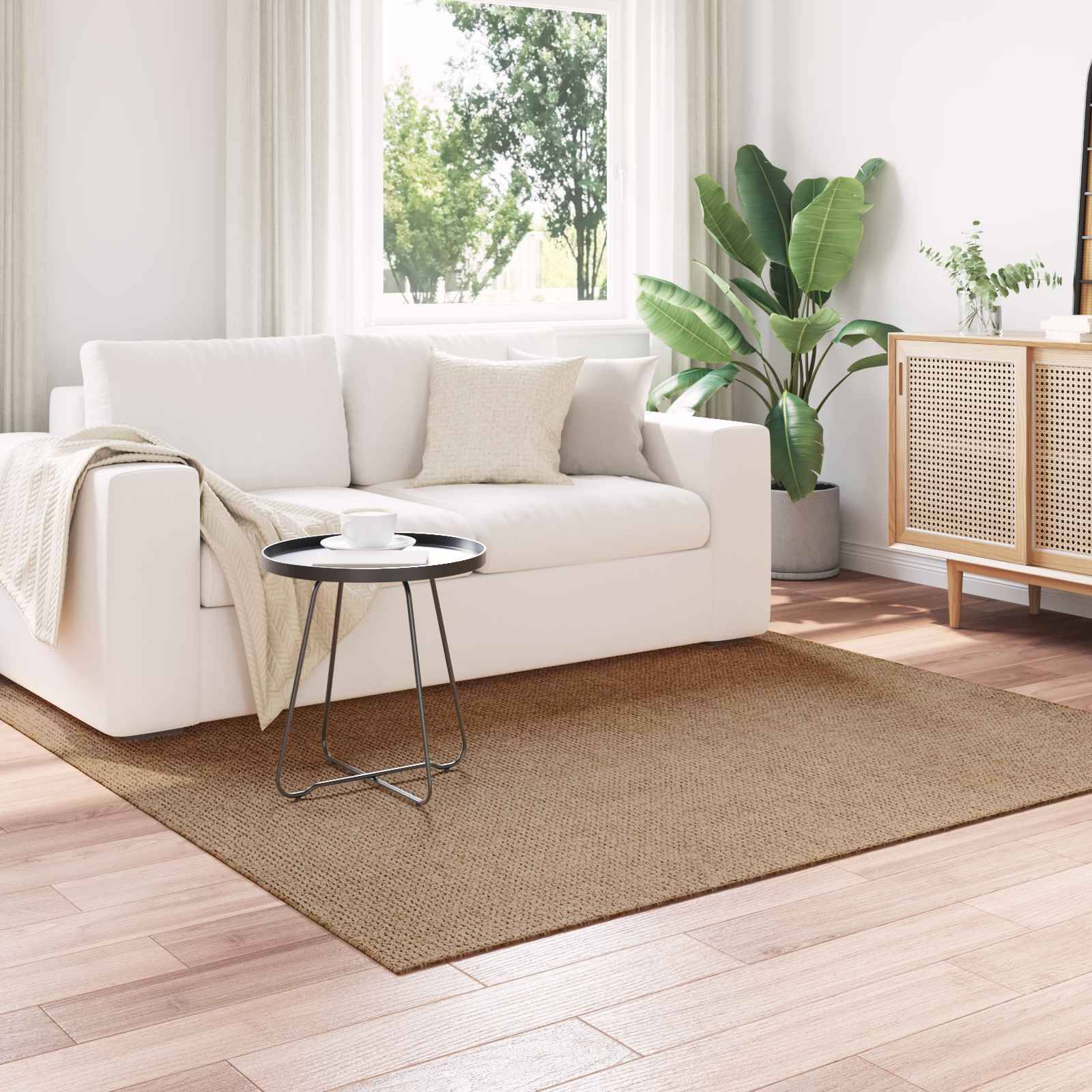 Ein helles, minimalistisches Wohnzimmer mit einem weißen Sofa, kleinem schwarzen Tisch, grünen Pflanzen und einem Holzschrank auf hellem Holzboden.