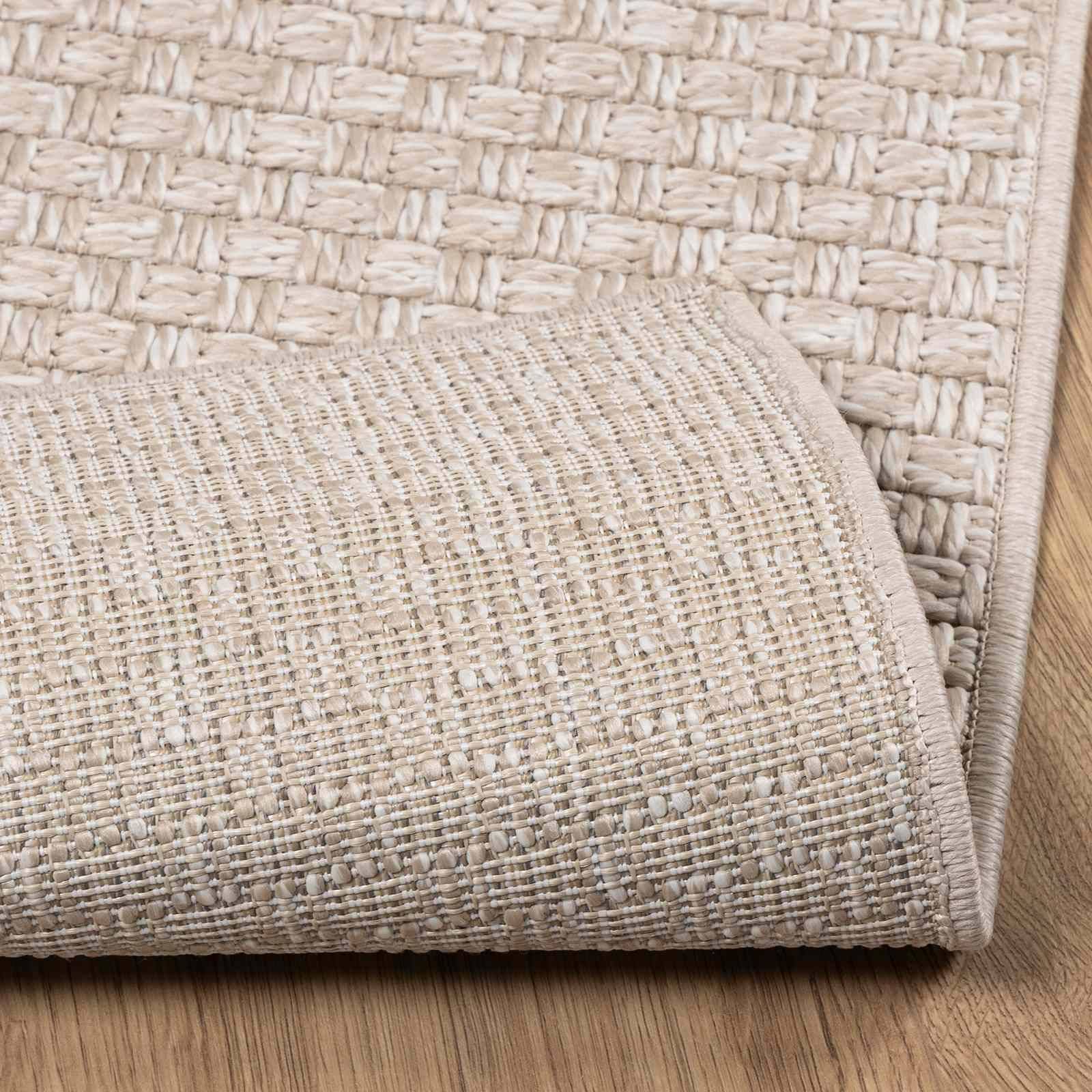 Ein beiger gewebter Teppich mit einfachem Muster ist teilweise zurückgefaltet und zeigt einen hellen Holzboden. Das Bild hebt die Textur des Teppichs hervor.