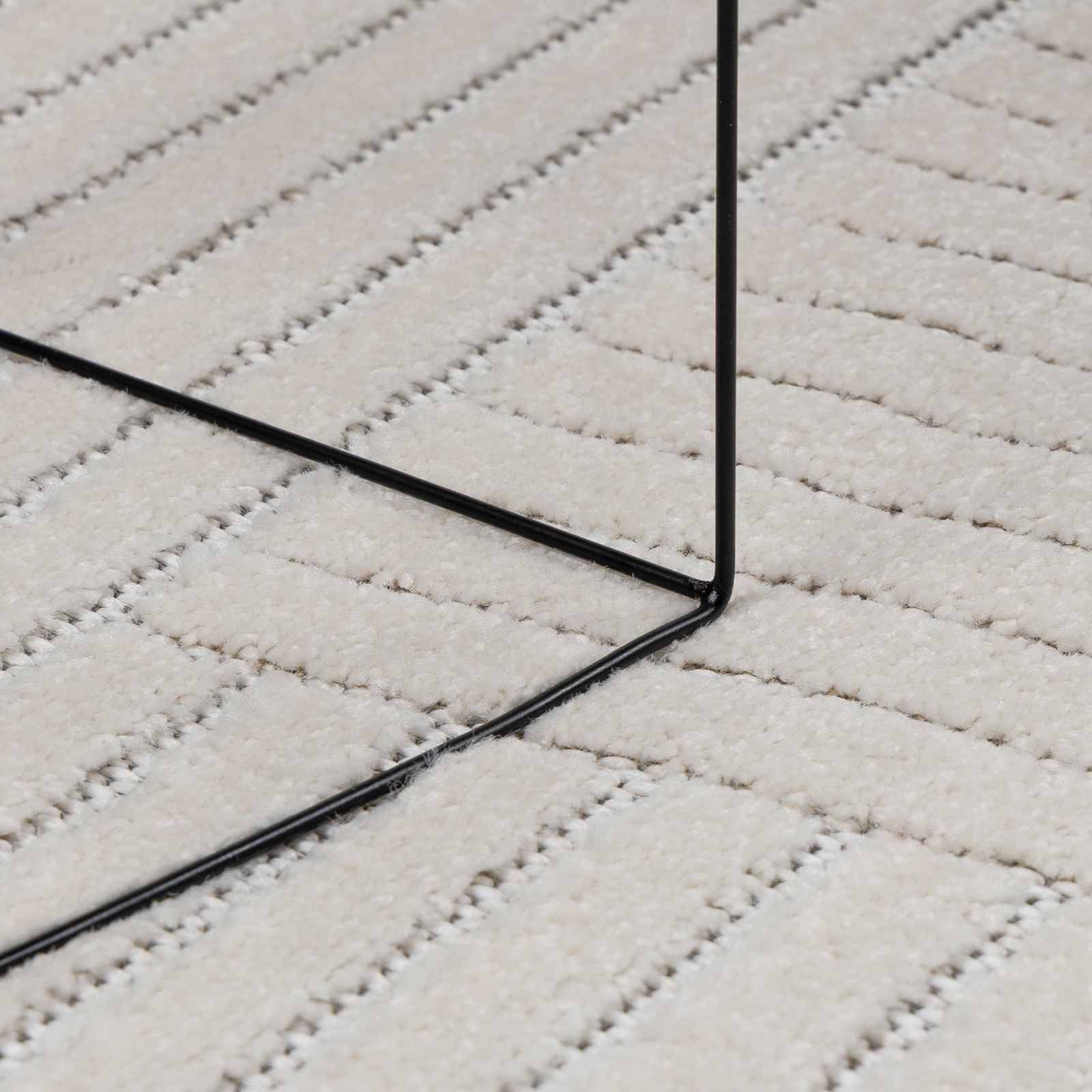 Eine Nahaufnahme einer schwarzen Metallrahmenecke auf einem beigen, strukturierten, gestreiften Teppich.