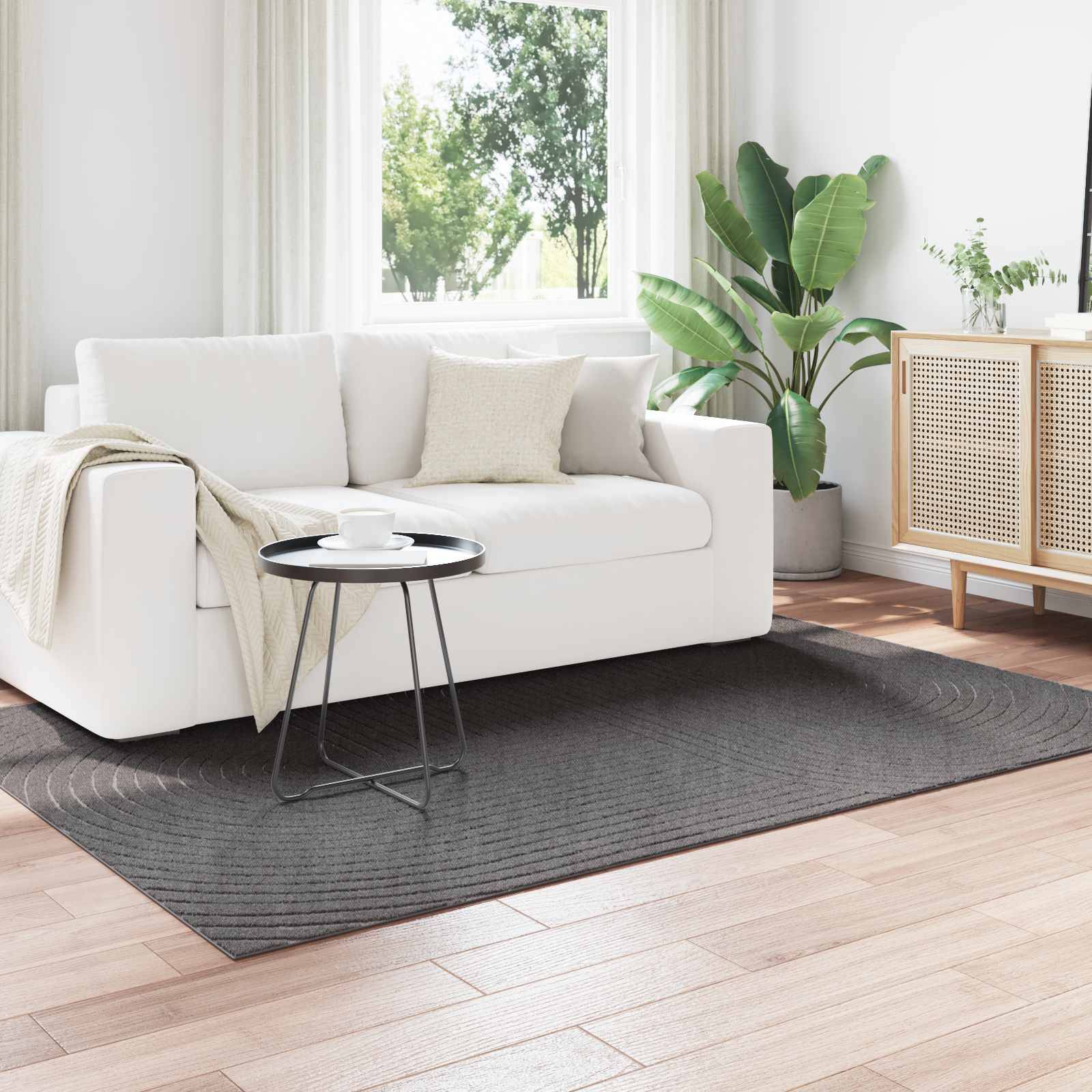 Ein modernes Wohnzimmer mit weißem Sofa, schwarzem Beistelltisch und Pflanzen, mit einem großen Fenster, durch das natürliches Licht den Raum durchflutet.