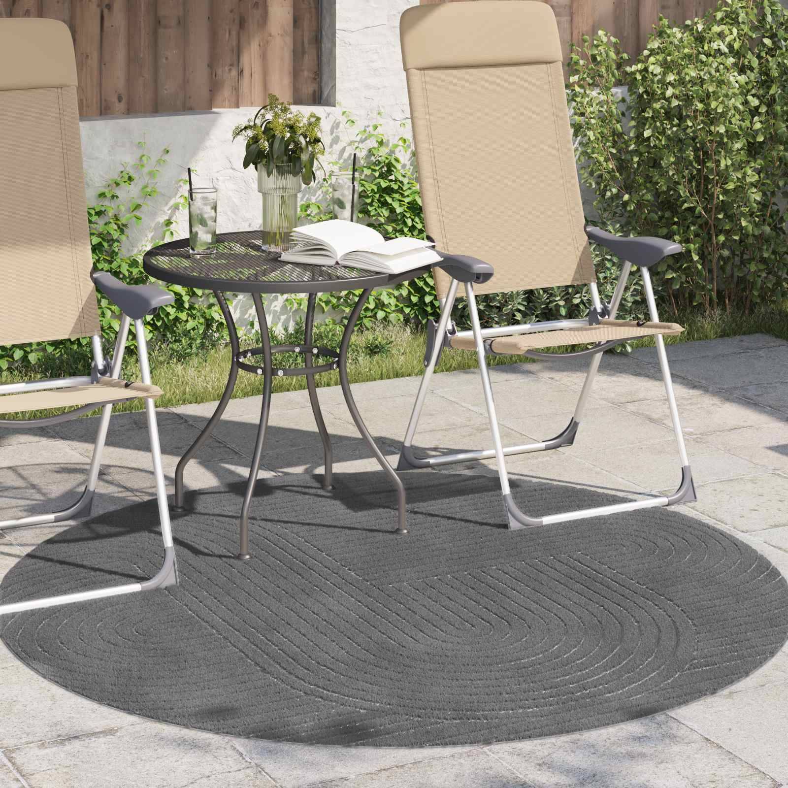 Zwei beige Terrassenstühle und ein kleiner runder Tisch mit einem aufgeschlagenen Buch und einer Topfpflanze, angeordnet auf einem grauen Außenteppich in einer Gartenterrassensetting.