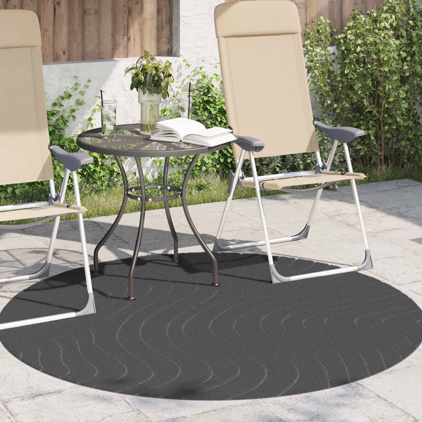 Zwei beige Liegestühle und ein kleiner Metalltisch mit einem Buch und einer Vase stehen auf einem gemusterten Outdoor-Teppich auf einer Terrasse.