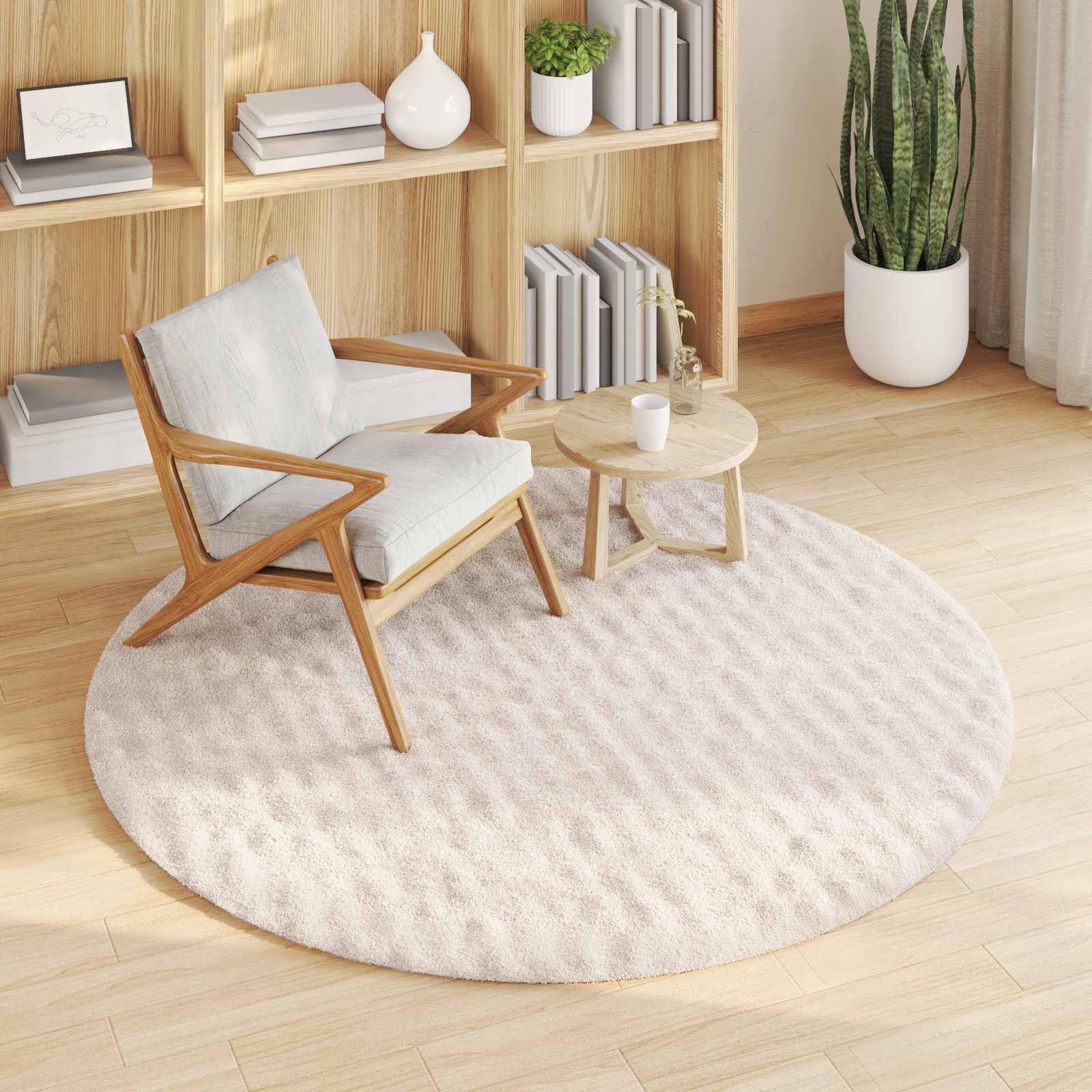 Ein gemütlicher Wohnraum mit einem Holzsessel mit hellem Kissen, der auf einem runden beigen Teppich steht, neben einem kleinen Holztisch. Im Hintergrund befinden sich Regale mit Büchern und Pflanzen.