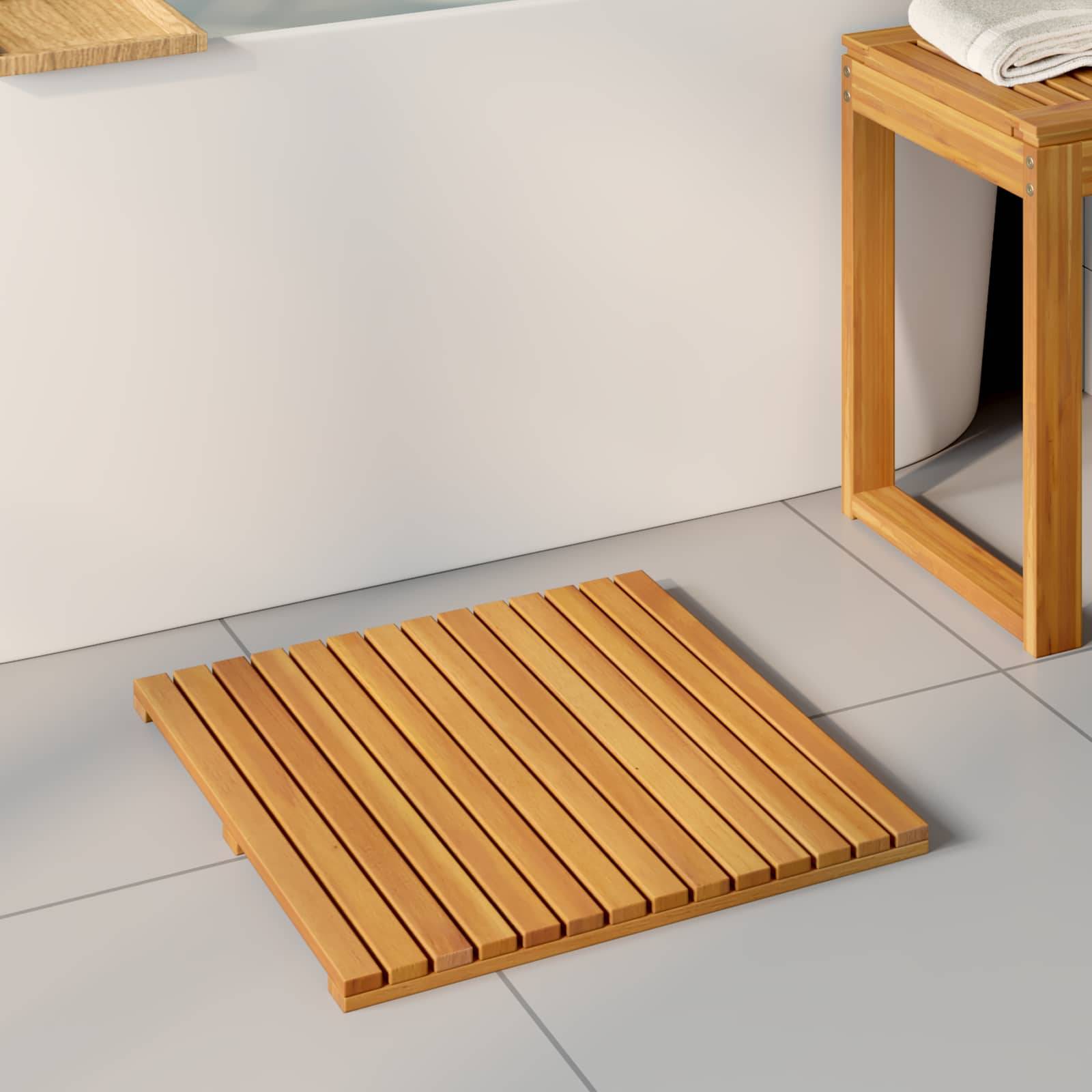 Eine Badematte aus Holz mit Lamellenentwurf auf einem gefliesten Badezimmerboden, neben einem Holzhocker mit gefalteten Handtüchern oben drauf.