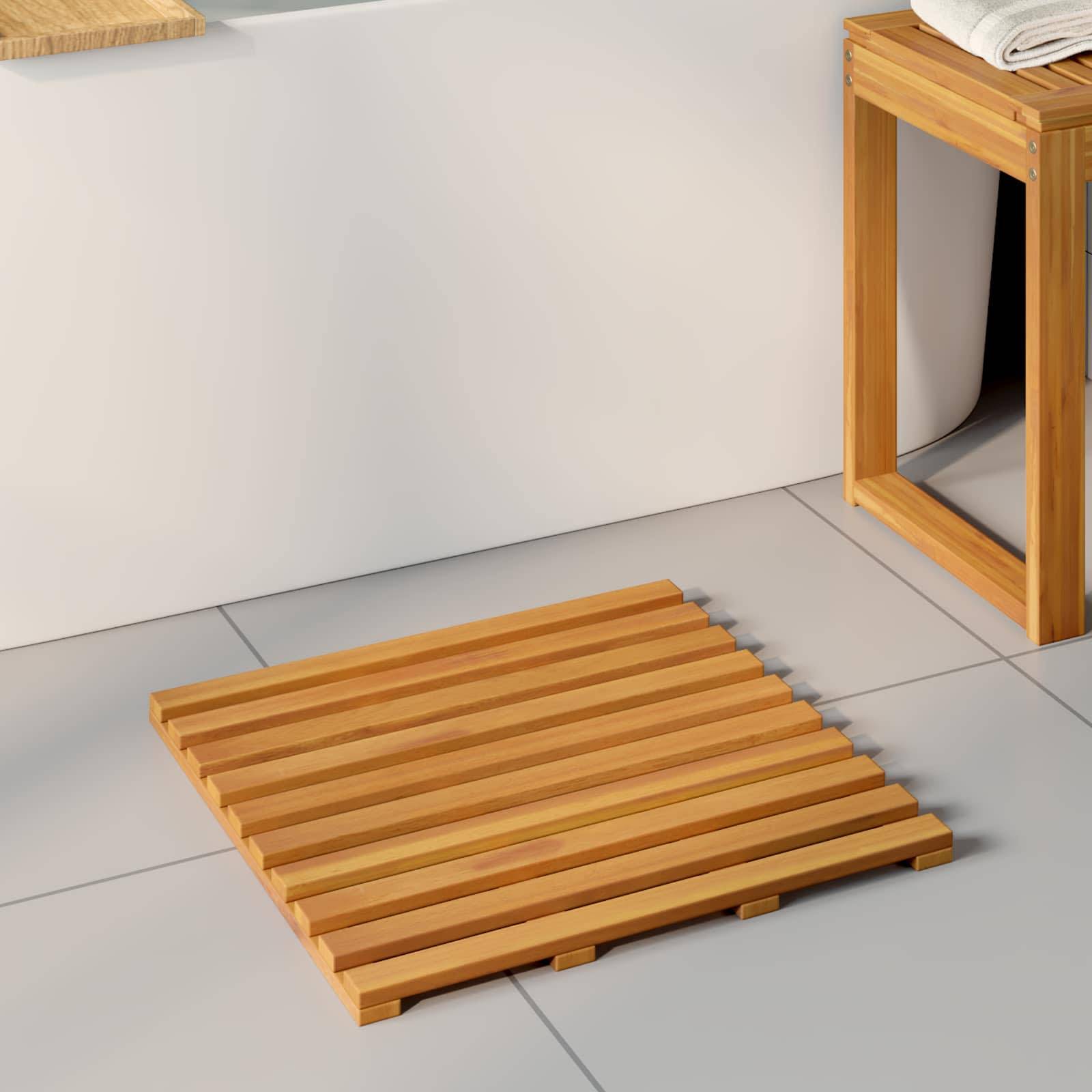 Eine Holzlattenmatten wird auf einem gekachelten Badezimmerboden neben einem Holzhocker mit gefalteten weißen Handtüchern oben platziert.