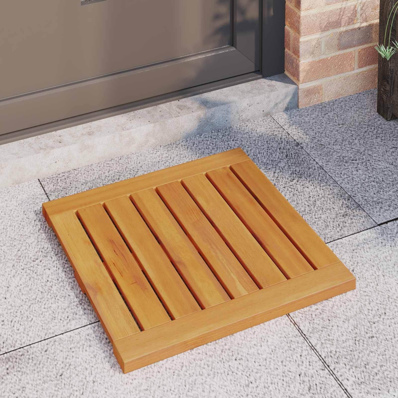 Eine hölzerne Fußmatte liegt auf einem gefliesten Außenweg neben einer Backsteinmauer und einer Tür. Die Matte hat gleichmäßig verteilte Latten und eine helle Oberflächenfinish.
