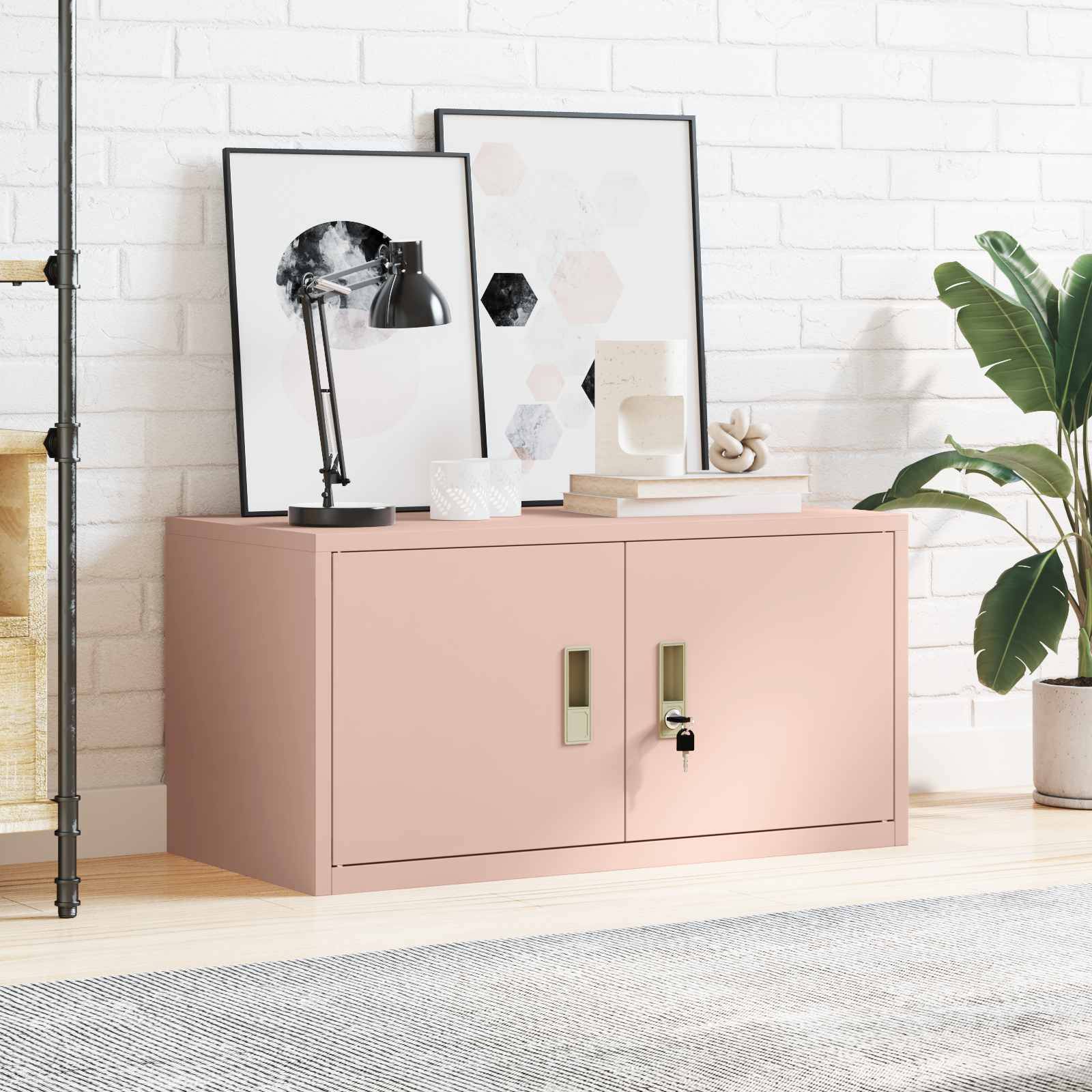 Ein Wohnzimmer mit einem rosa Aufbewahrungsschrank, gerahmter Kunst, einer Lampe und einer Pflanze an einer weißen Backsteinwand, die eine gemütliche Atmosphäre schafft.