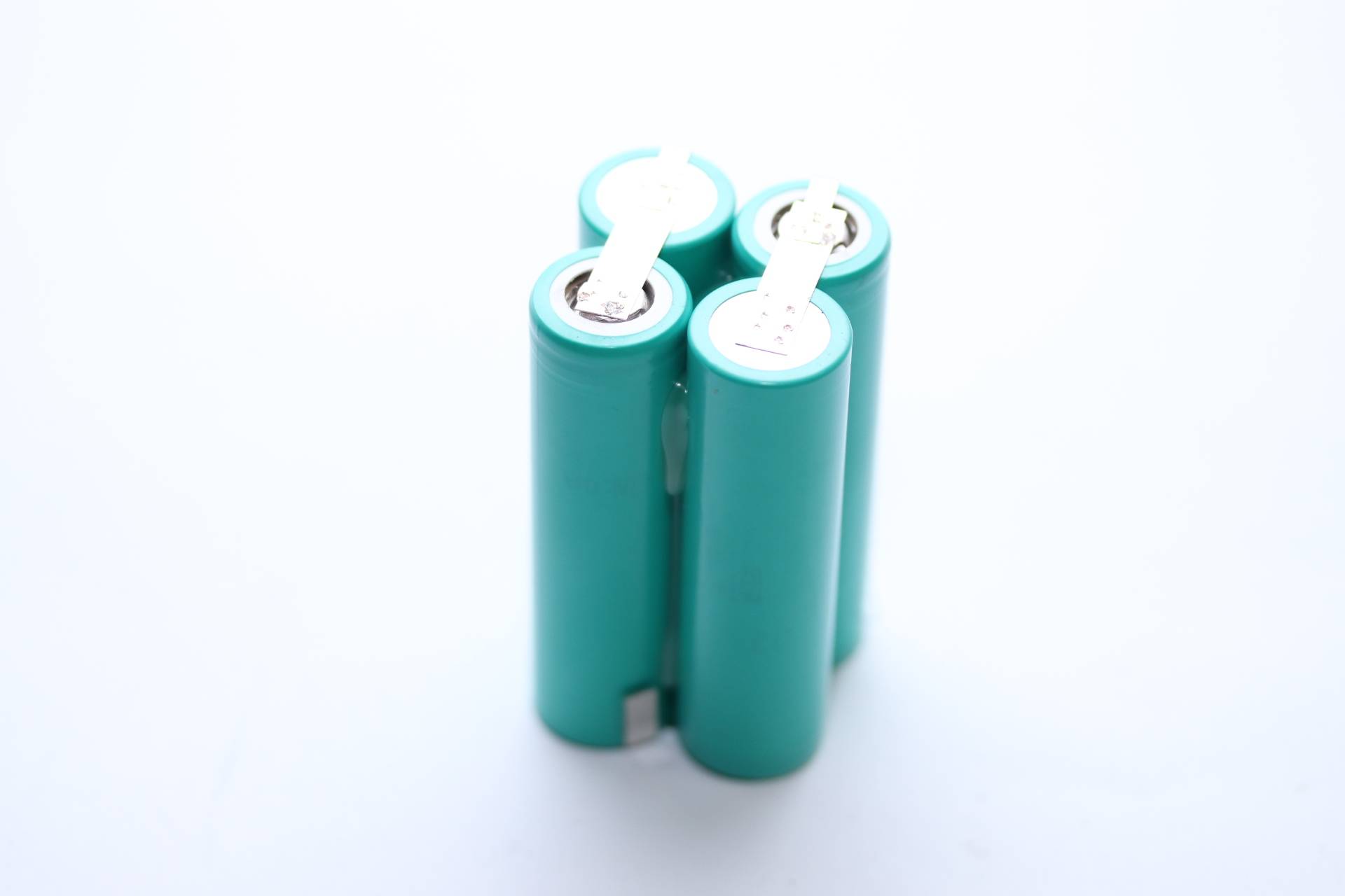 Vier türkisfarbene zylindrische Batterien, die zusammen gruppiert sind und aufrecht gegen einen hellen Hintergrund stehen.