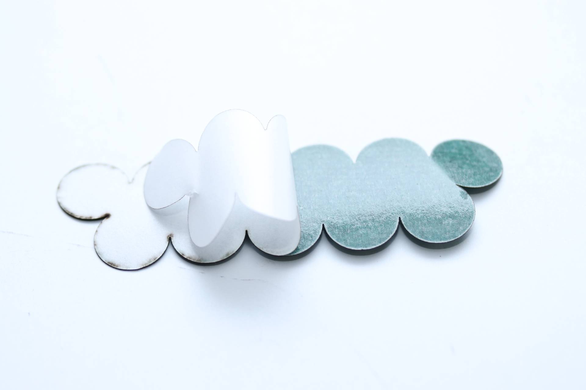 Eine Nahaufnahme einer ausgeschnittenen Form, die abgerundeten Wolken ähnelt, aus Papier gefertigt, mit gemischten weißen und blaugrünen Farben, teilweise gefaltet.