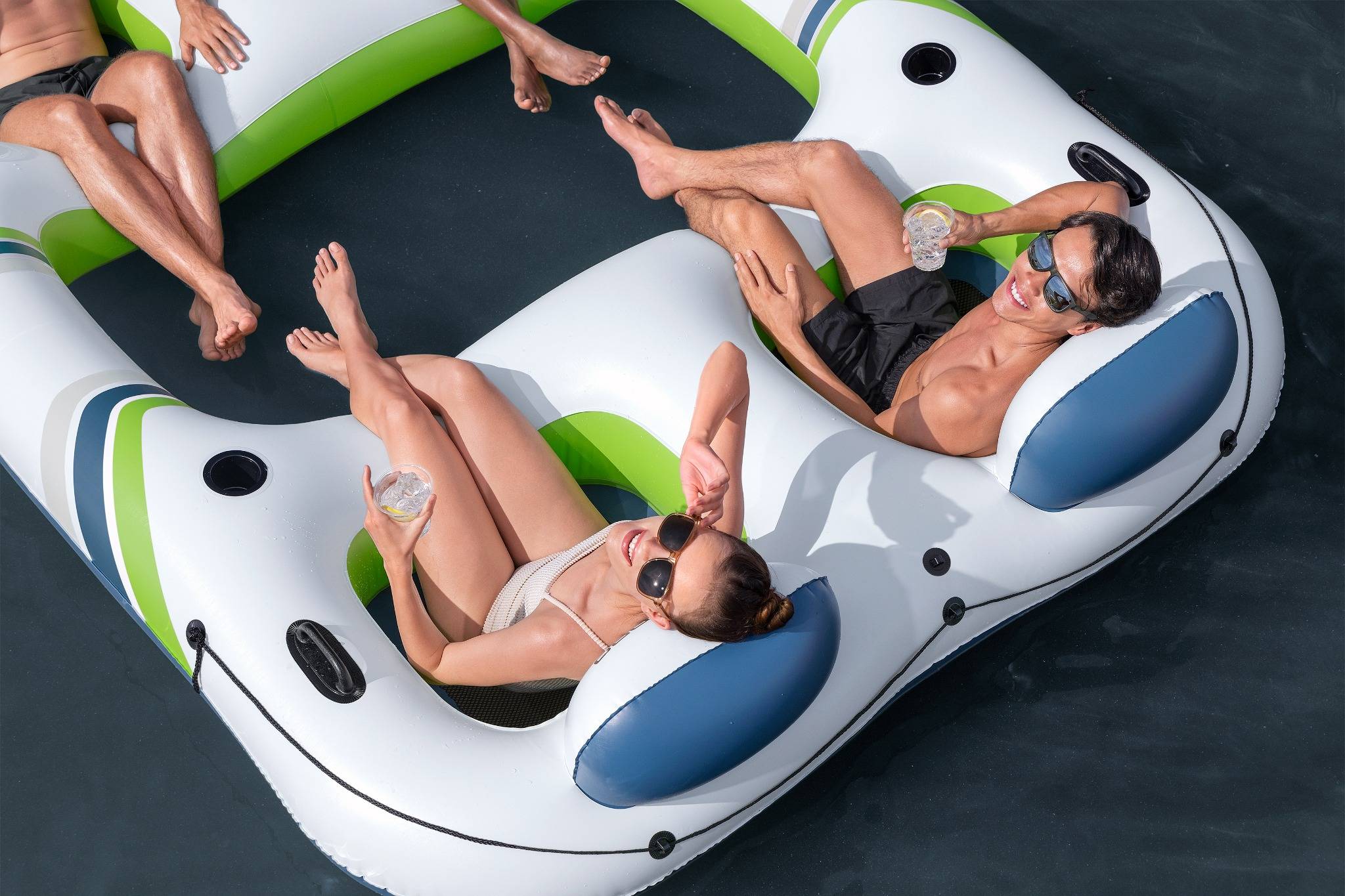 Zwei Personen entspannen sich auf einem aufblasbaren Floß in einem Pool, halten Getränke in den Händen und genießen das helle Sonnenlicht.