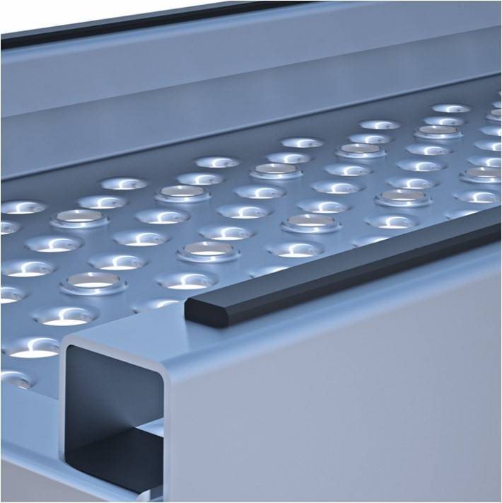 Nahaufnahme einer silbernen Metalloberfläche mit erhabenen kreisförmigen Noppen und einer schwarzen Kante, die die rutschfeste Textur und das Design hervorhebt.