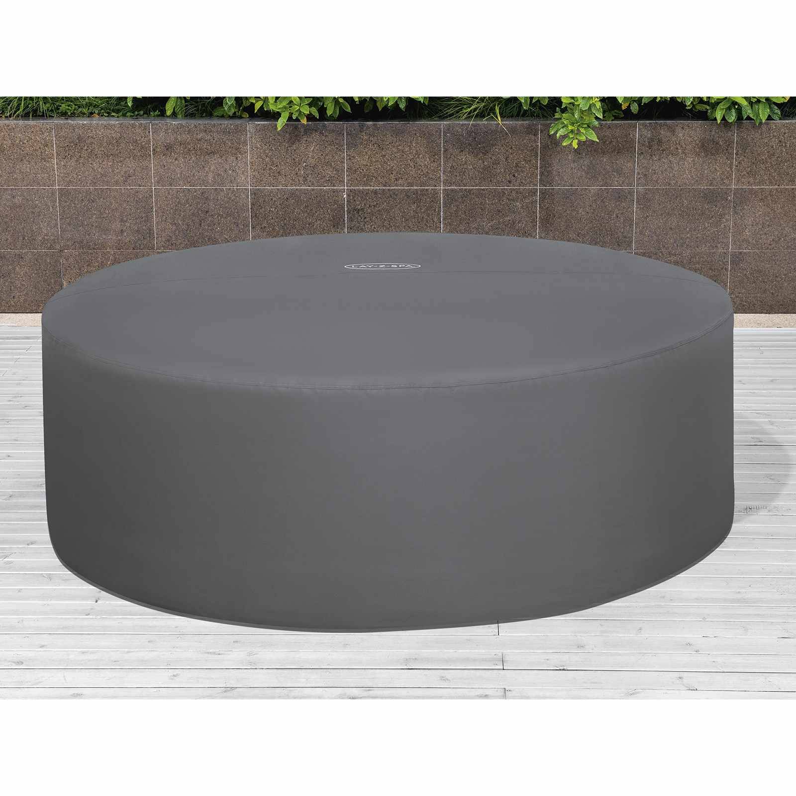Großer runder grauer gepolsterter Hocker oder Plattformtisch auf einer weißen Terrasse, mit einer Steinmauer und Grünflächen dahinter.
