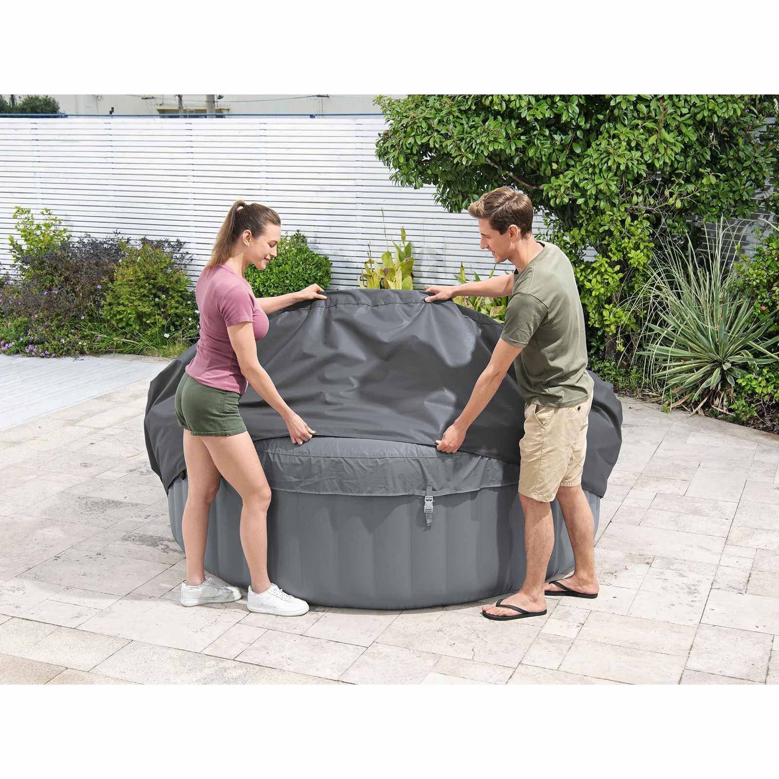 Zwei Personen bringen eine Schutzabdeckung über einem Outdoor-Whirlpool auf einer Hinterhofdeck an.