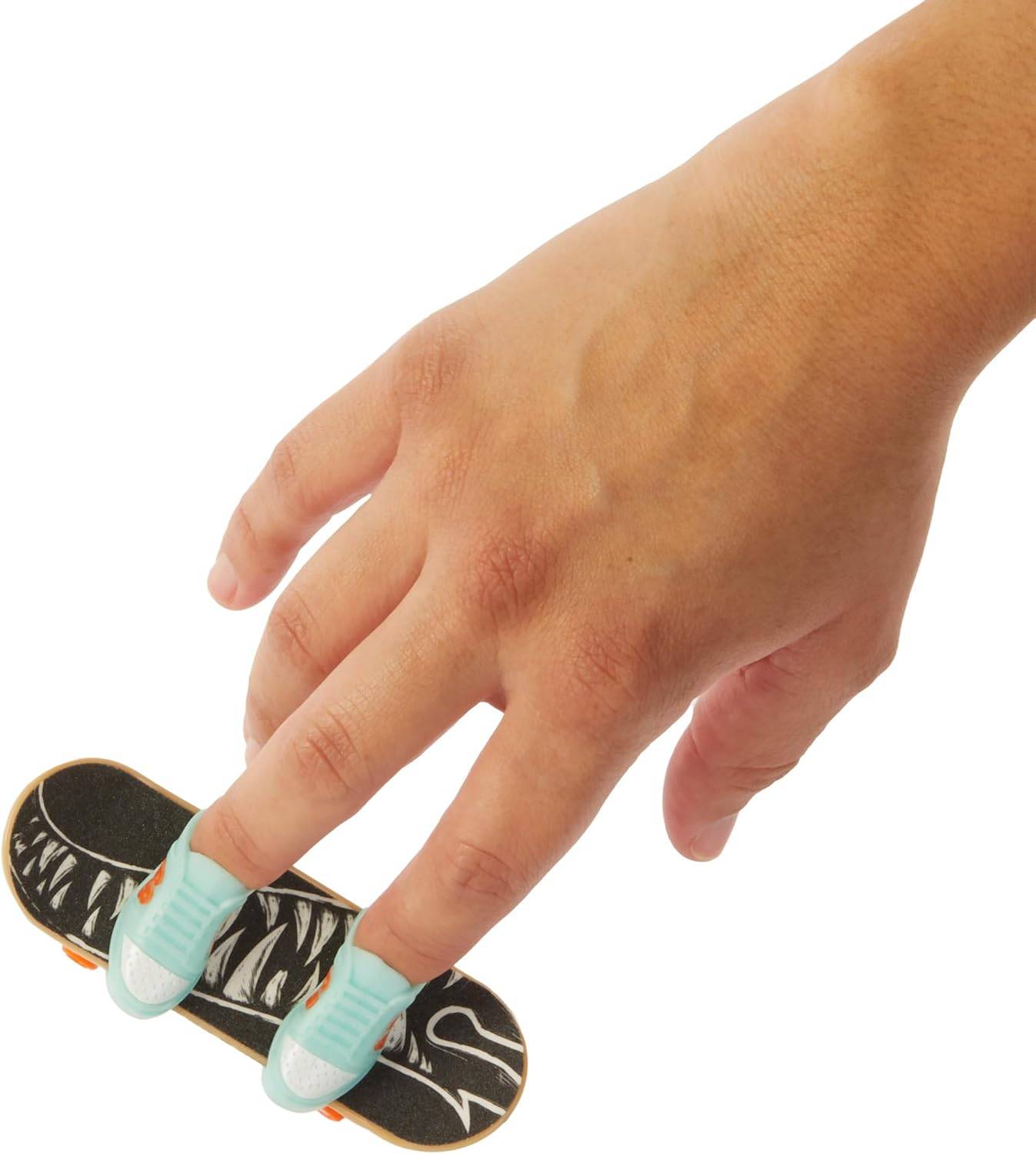 Eine Hand führt einen Skateboard-Trick mit Fingern auf einem Miniatur-Skateboard mit petrolblauen Schuhen auf einem gemusterten schwarzweißen Brett auf.