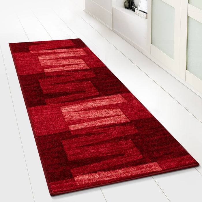 Ein rechteckiger rot und kastanienbraun gemusterter Teppich liegt auf einem weißen Boden neben einem hellfarbigen Schrank und verleiht einem modernen Innenraum Wärme.
