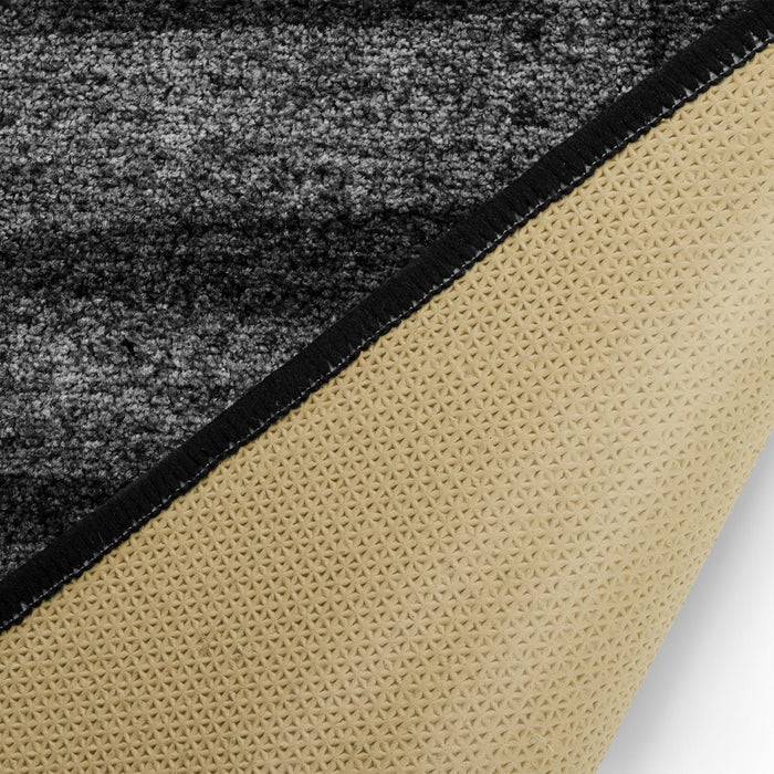 Nahaufnahme einer grau und schwarz strukturierten Teppichekke, umgeklappt, um eine beige rutschfeste Rückseite mit einem Dreiecksmuster zu zeigen.