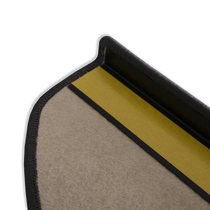 Eine Nahaufnahme der Kante einer Autofußmatte, die eine geschichtete Konstruktion mit beigem Teppich, einer schwarzen Bordüre und einem gelben Rückenmaterial zeigt.