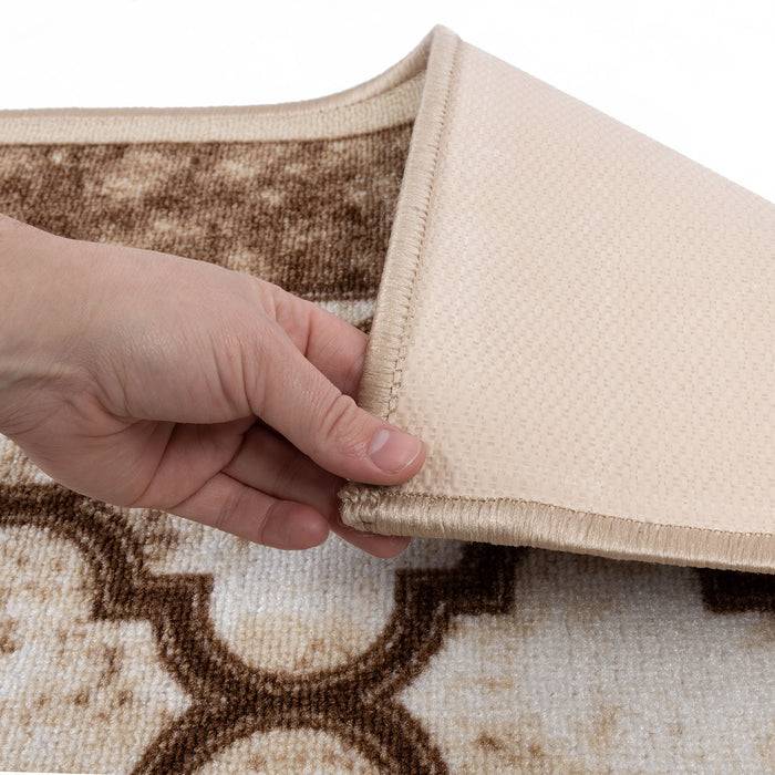 Eine Hand hebt die Ecke eines beige und braun gemusterten Teppichs, wobei die rutschfeste Rückseite darunter sichtbar wird.