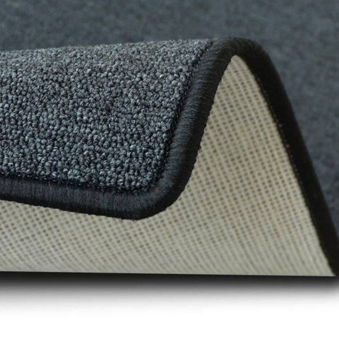 Eine Nahaufnahme einer grauen Teppichecke, die das strukturierte Gewebe oben und die rutschfeste Unterseite darunter zeigt.