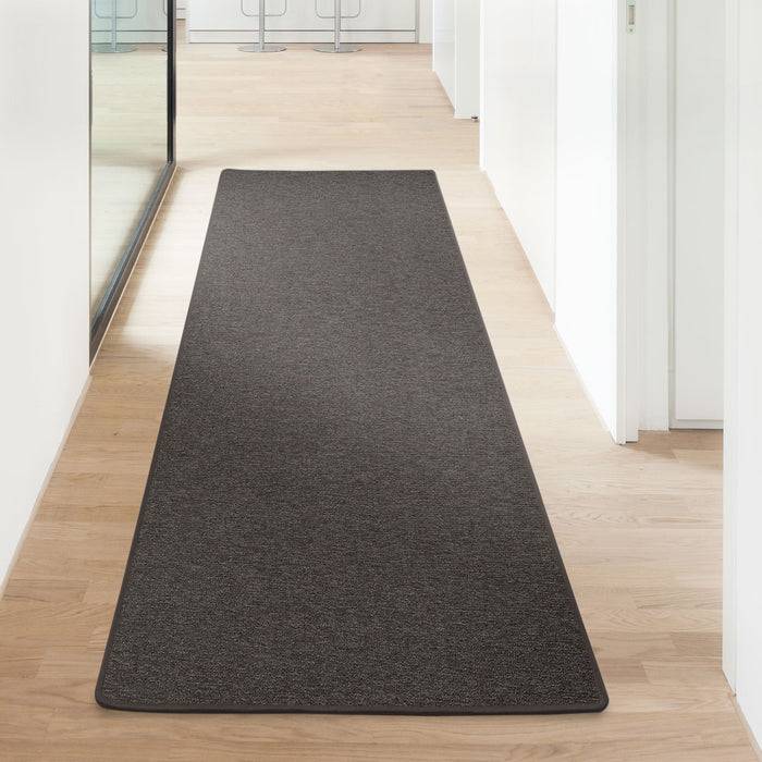 Dunkler Flurläufer auf hellem Holzboden zwischen weißen Wänden und Glasfenster, der zu Barhockern am anderen Ende führt.