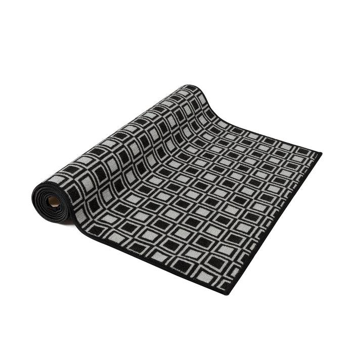 Ein schwarz-weißer Teppich mit einem sich wiederholenden quadratischen geometrischen Muster ist teilweise ausgerollt und wird vor einem schlichten weißen Hintergrund präsentiert.