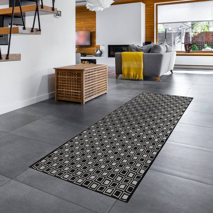Ein modernes Wohnzimmer mit einem geometrisch gemusterten Teppich auf grauem Fliesenboden, einem grauen Sofa mit gelben Akzenten und Holzdekor-Elementen.