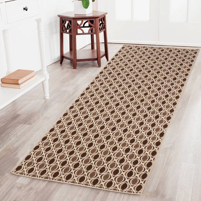 Ein Flur mit einem gemusterten Teppich mit kreisförmigen Designs in Braun- und Beigetönen, der zu einem kleinen Holztisch mit einer Topfpflanze führt.