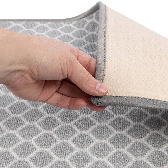 Eine Hand hebt die Ecke eines grau-weiß gemusterten Teppichs an und zeigt seine strukturierte Rückseite.