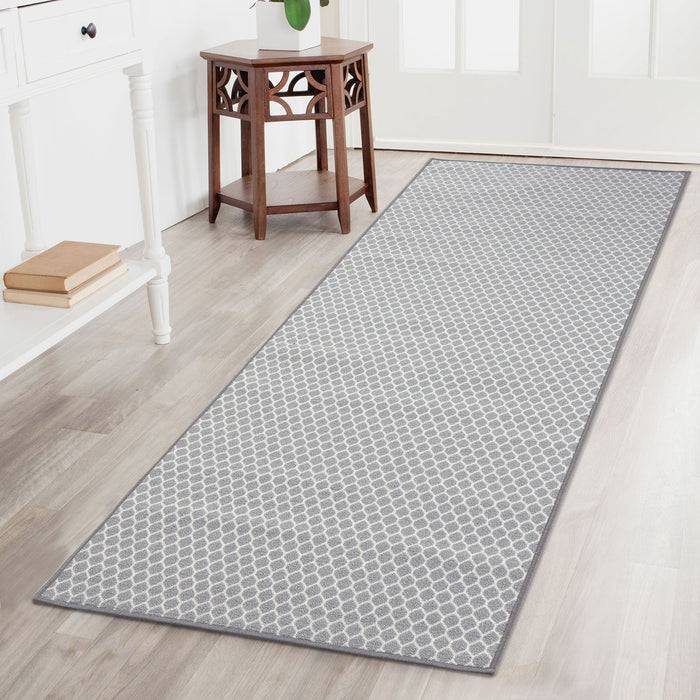 Ein langer, grau gemusterter Teppich auf einem Hartholzboden, der zu einem kleinen Holztisch mit einer Pflanze führt, vor einer weißen Wand mit Büchern.