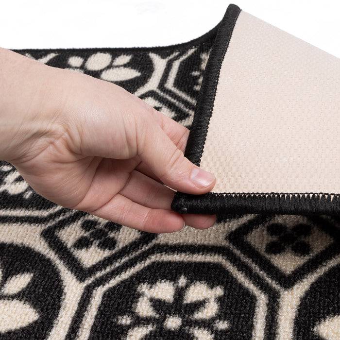 Eine Hand hebt die Ecke eines schwarz-beigen gemusterten Teppichs an und zeigt die Textur und die Unterseite.