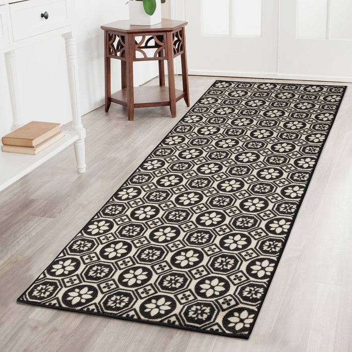 Ein schwarzweißes gemusterter Teppich mit sechseckigen Blumendesigns verläuft über einen hellarbigen Boden in einem hellen Raum mit weißen Möbeln.